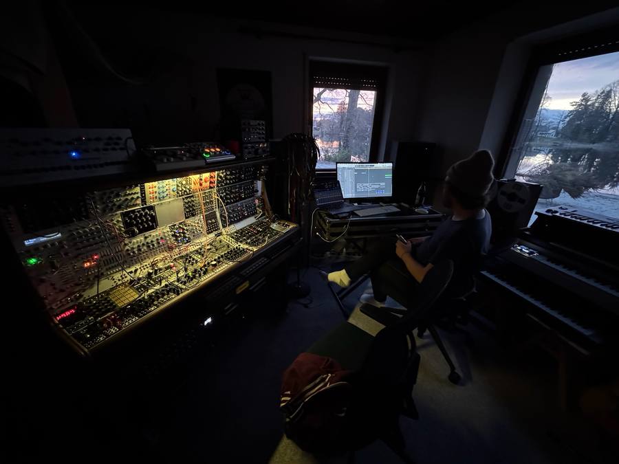 Dark studio at dusk, modular wall glowing, lake outside the window