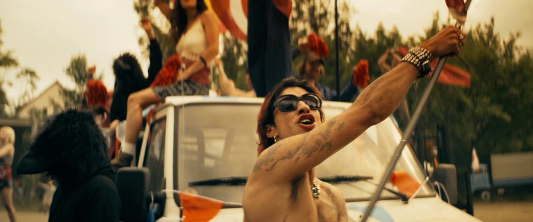Performer with sunglasses on a car, crowd waving flags behind